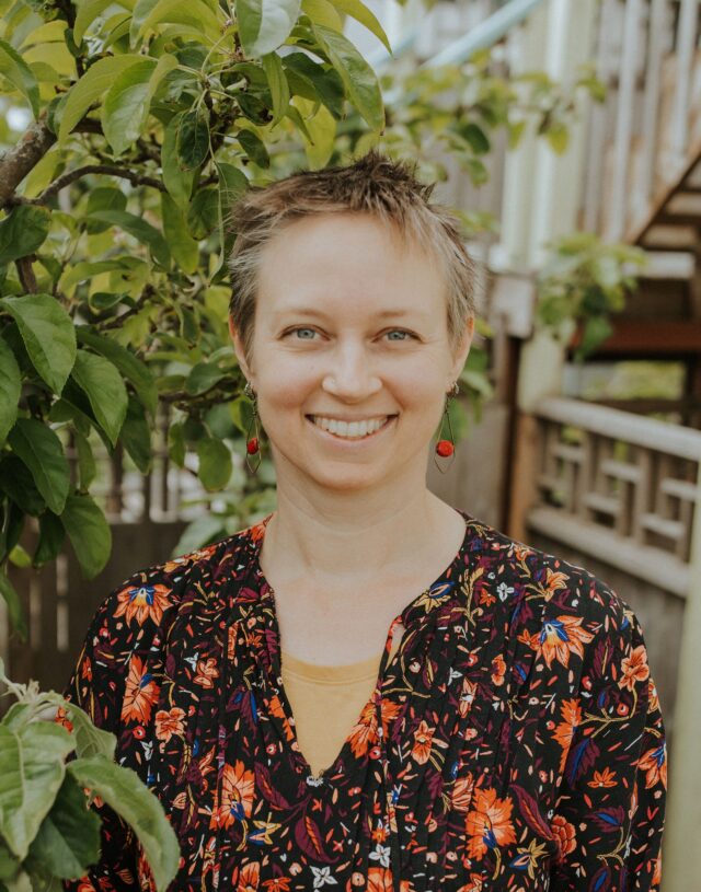 A close up photo of Karin Lamberson with stairs and a bush in the background.